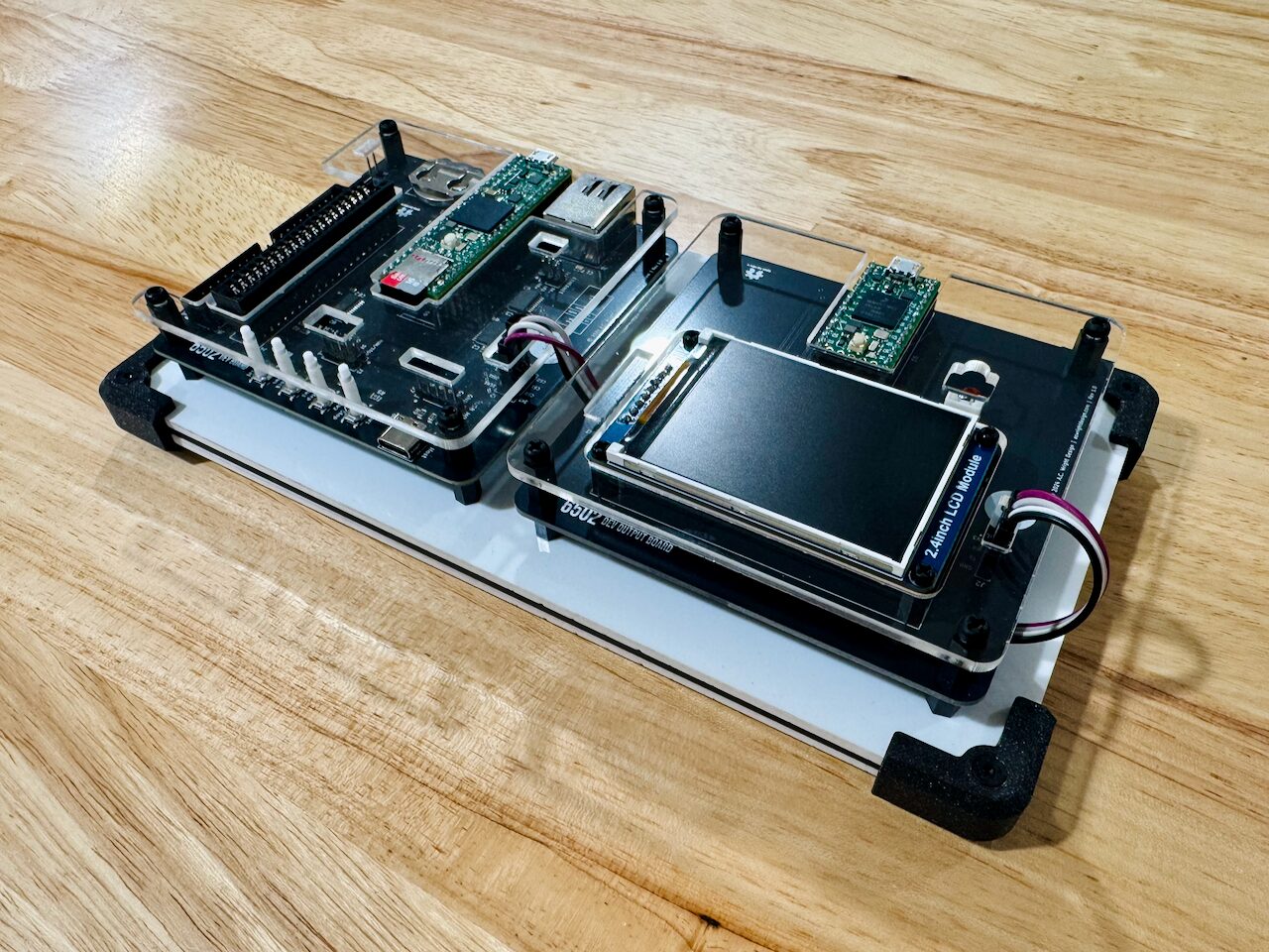 Two boards side by side on a plate: one with a Teensy module and a row of four buttons, the other carrying a small color LCD.
